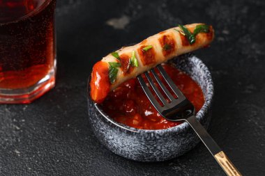 Lezzetli ızgara sosisli çatal ve siyah arka planda bir kase sos.