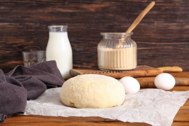 Ahşap arka planda taze hamurlu kağıt, yumurta ve süt şişesi.