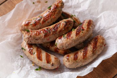 Ahşap arka planda lezzetli ızgara sosislerle pişirilmiş kağıt, yakın plan.