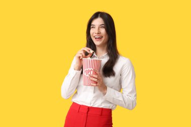 Sarı arka planda patlamış mısır yiyen genç bir kadın.