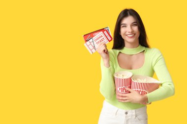 Patlamış mısır kovaları ve sarı arka planda biletleri olan şok olmuş genç bir kadın.