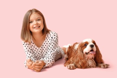 Kral Charles 'ın köpeğiyle pembe arka planda yatan tatlı küçük kız.