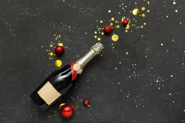 Bir şişe şampanya ve siyah arka planda konfeti.