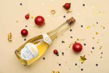 Bir şişe şampanya, Noel topları ve bej arka planda konfeti.