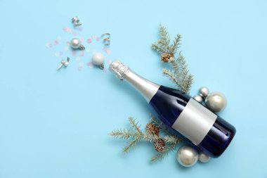 Bir şişe köknar dallı şampanya, Noel baloları ve mavi arka planda konfeti.