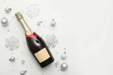 Bir şişe şampanya, beyaz arka planda Noel topları, kar taneleri ve konfeti.