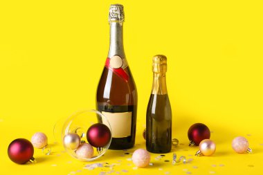 Cam şişeli şampanya, Noel topları ve sarı arka planda konfeti.