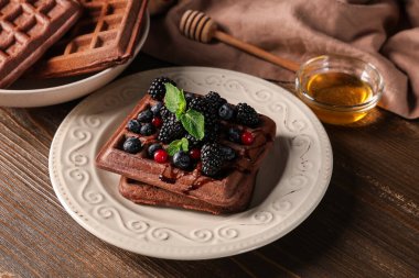 Taze böğürtlenli Belçika waffle tabağı ve ahşap zemin üzerinde bal.