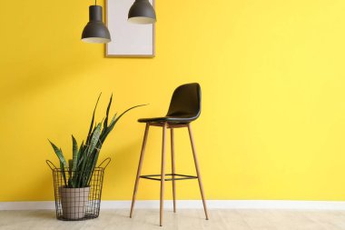 Çiçekli sandalye, asılı lamba ve çerçeveli sarı duvar