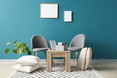 Sandalyeler, yerdeki yastıklar, kutularla dolu kahve masası ve mavi duvarın yanındaki oda.