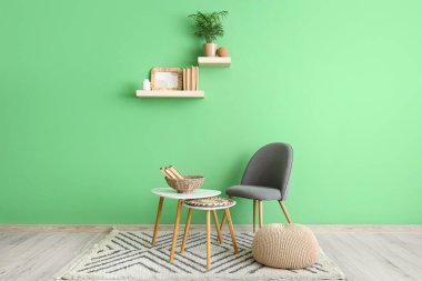 Sandalye, puf, sehpa ve yeşil duvarlı raflar.