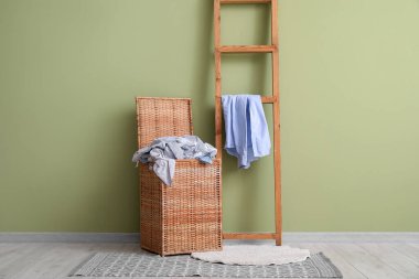 Kirli giysiler ve yeşil duvarın yanında merdiven olan hasır çamaşır sepeti.