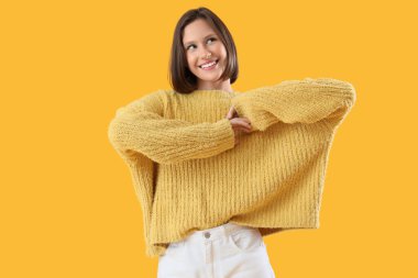 Sarı arka planda kalın kazaklı genç bir kadın.