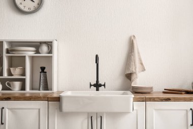 Ahşap tezgahta lavabo ve mutfaktaki beyaz duvarın yanında raf ünitesi.