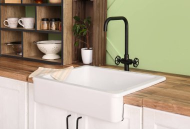 Beyaz seramik lavabo ve raf ünitesi mutfaktaki yeşil duvarın yanındaki ahşap tezgahta.