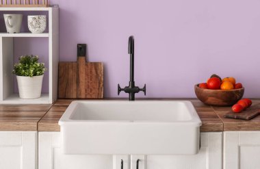 Beyaz seramik lavabo ve sebze kasesi mutfaktaki mor duvarın yanındaki ahşap tezgahta.