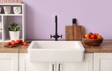 Beyaz seramik lavabo ve sebze kasesi mutfaktaki mor duvarın yanındaki ahşap tezgahta.