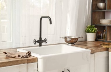 Rahat mutfağın penceresinin yanındaki ahşap tezgahta beyaz seramik lavabo.