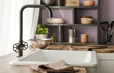 Beyaz seramik lavabo ve raf ünitesi mutfaktaki mor duvarın yanındaki ahşap tezgahın üzerinde.