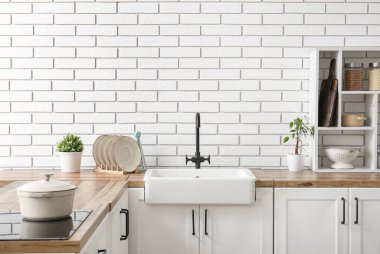 Beyaz seramik lavabo ve raf ünitesi mutfaktaki beyaz tuğla duvarın yanındaki ahşap tezgahta.