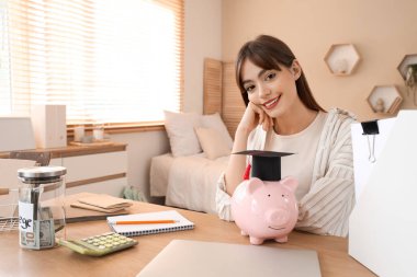 Masasında domuz kumbarası olan bir kız öğrenci. Eğitim tasarruf kavramı