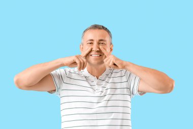 Mutlu olgun bir adam mavi arka planda yüz geliştirme egzersizi yapıyor.