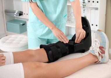 Kadın doktor klinikte kırık bir kadının bacağına sabitleyici takıyor.