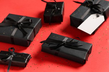 Kırmızı arka planda bir sürü siyah hediye kutusu ve konfeti.