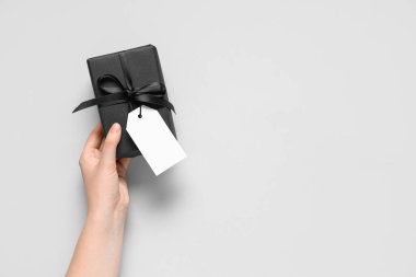 Gri arka planda siyah hediye kutusu olan bir kadın el.