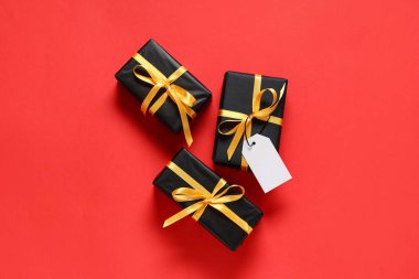 Kırmızı arka planda altın kurdeleli siyah hediye kutuları