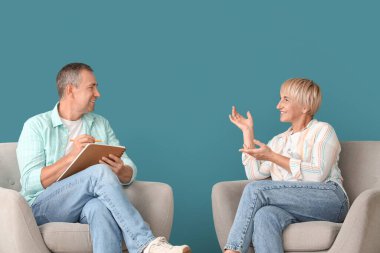 Yaşlı çift koltuklarda oturuyor ve mavi duvarın yanında konuşuyor.