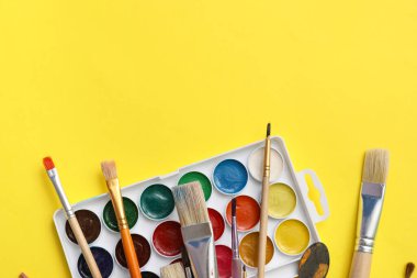 Sanatçı sarı arka planda fırçalar ve boyalar
