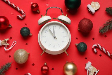 Alarmlı saat, dekorasyon, şeker kamışı ve kırmızı arka planda konfeti kompozisyonu. Noel geri sayımı konsepti. Üst görünüm