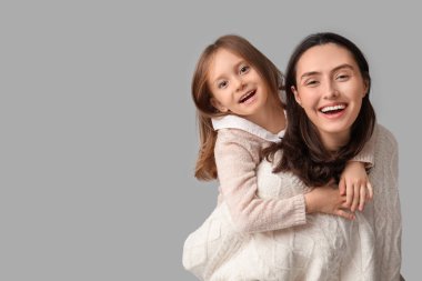 Genç anne küçük kızını gri arka planda sırtında taşıyor.