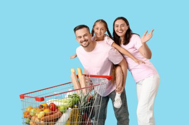 Alışveriş arabalı mutlu aile mavi arka planda eğleniyor.
