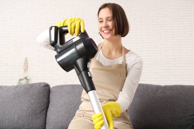 Evdeki koltukta oturan modern elektrikli süpürgeyle güzel bir genç kadın.