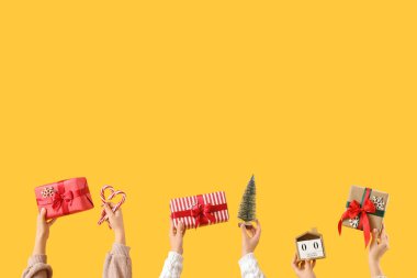 Noel hediyeli kadın elleri, küp takvimi, küçük köknar ağacı ve sarı arka planda şeker kamışı.