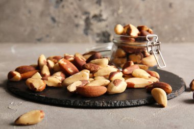 Siyah tahta ve kavanoz, gri arka planda lezzetli Brezilya fındıkları.