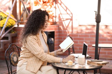 Dizüstü bilgisayarı ve not defteriyle sokak kafesindeki masada oturan genç Afro-Amerikalı yazar.