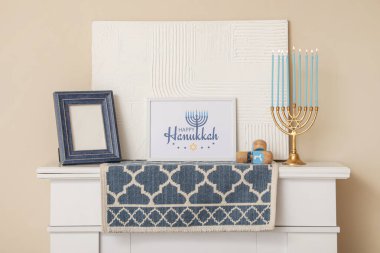 Fireplace with menorah, dreidels and greeting card near beige wall. Hanukkah celebration clipart