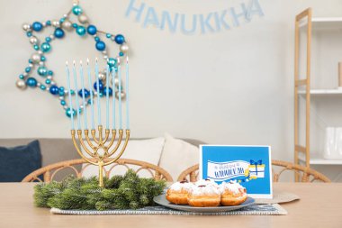 Dining table with menorah, wreath, donuts and greeting card in living room. Hanukkah celebration clipart