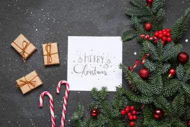 Noel kartı, hediyeler ve koyu arkaplanda süslenmiş köknar dallarıyla kompozisyon