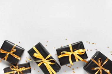 Altın kurdeleli siyah hediye kutuları ve gri arka planda konfeti.