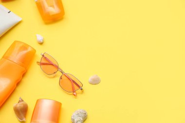 Sarı zemin üzerinde güneş kremi, deniz kabuğu ve güneş gözlüğü olan kompozisyon