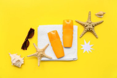 Sarı arka planda güneş kremi, havlu ve güneş gözlüğü şişeleriyle kompozisyon