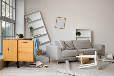 Depremden sonra kanepe, çekmece ve raf üniteleriyle dolu dağınık bir oturma odası.