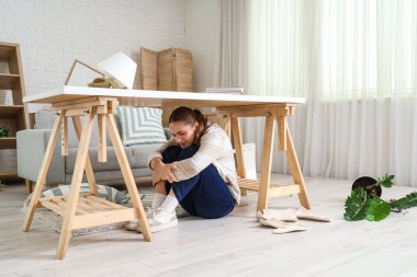 Deprem sırasında masanın altında saklanan korkmuş genç kadın.