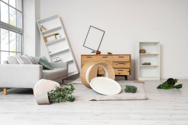 Kanepe, raf üniteleri ve deprem sonrası devrilen masalarla dolu dağınık bir oturma odası.