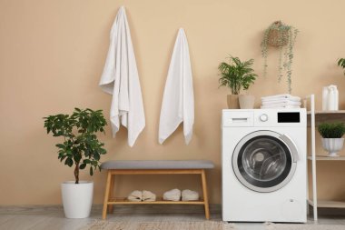 Çamaşır makinesi ve gri banklı şık bir banyo.