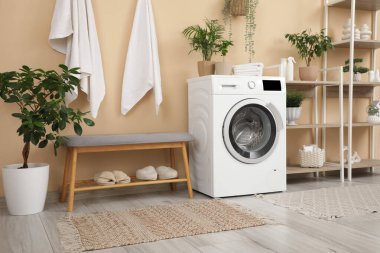 Rafların, çamaşır makinesinin ve gri bankın olduğu şık bir banyo.